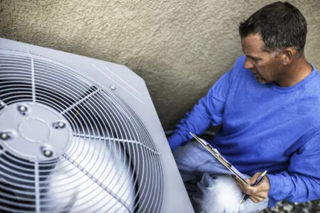 HVAC technician checking an outdoor unit with a clipboard