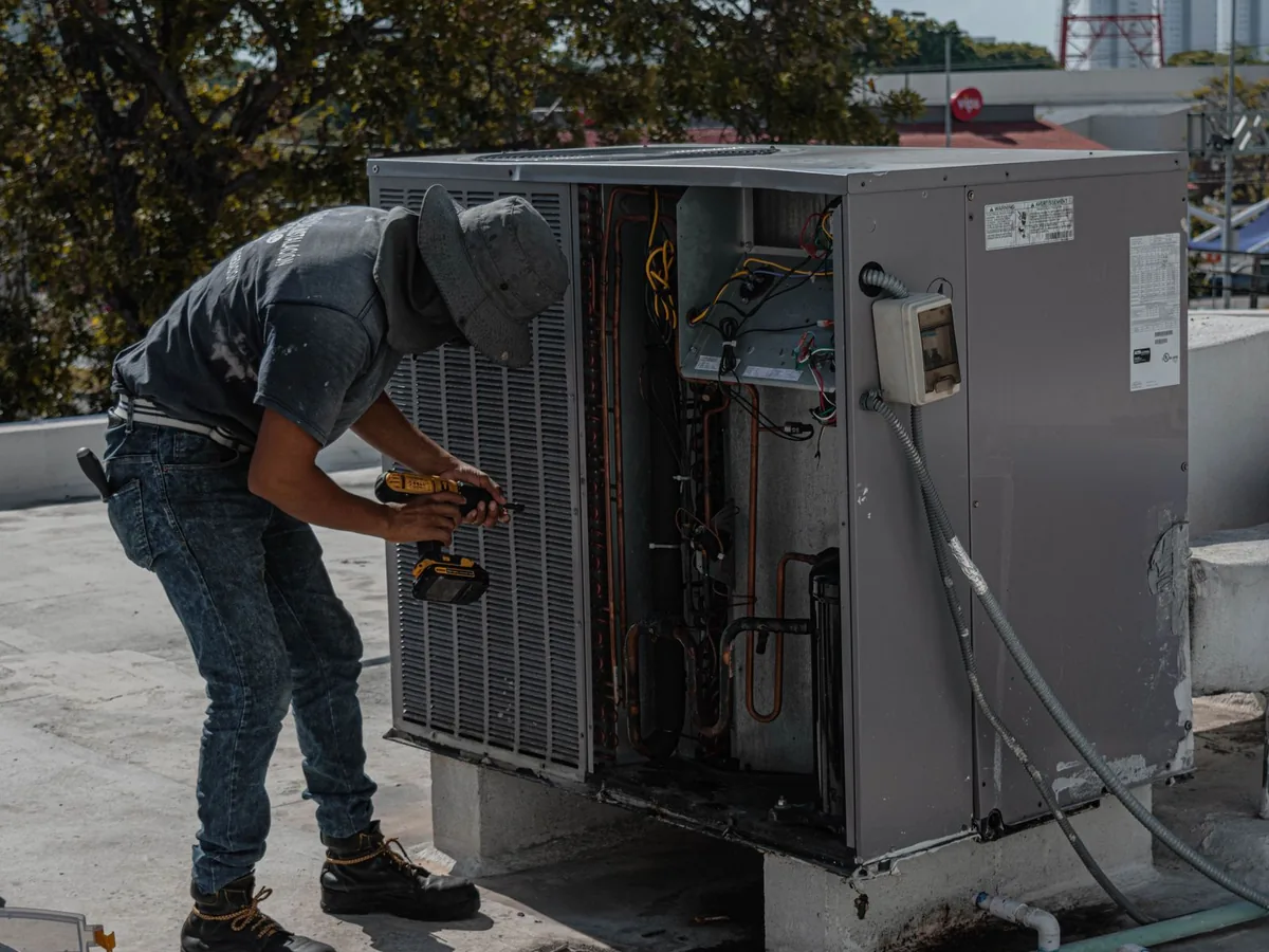 Technician inspecting the open panel of an outdoor air conditioning unit with a hand tool